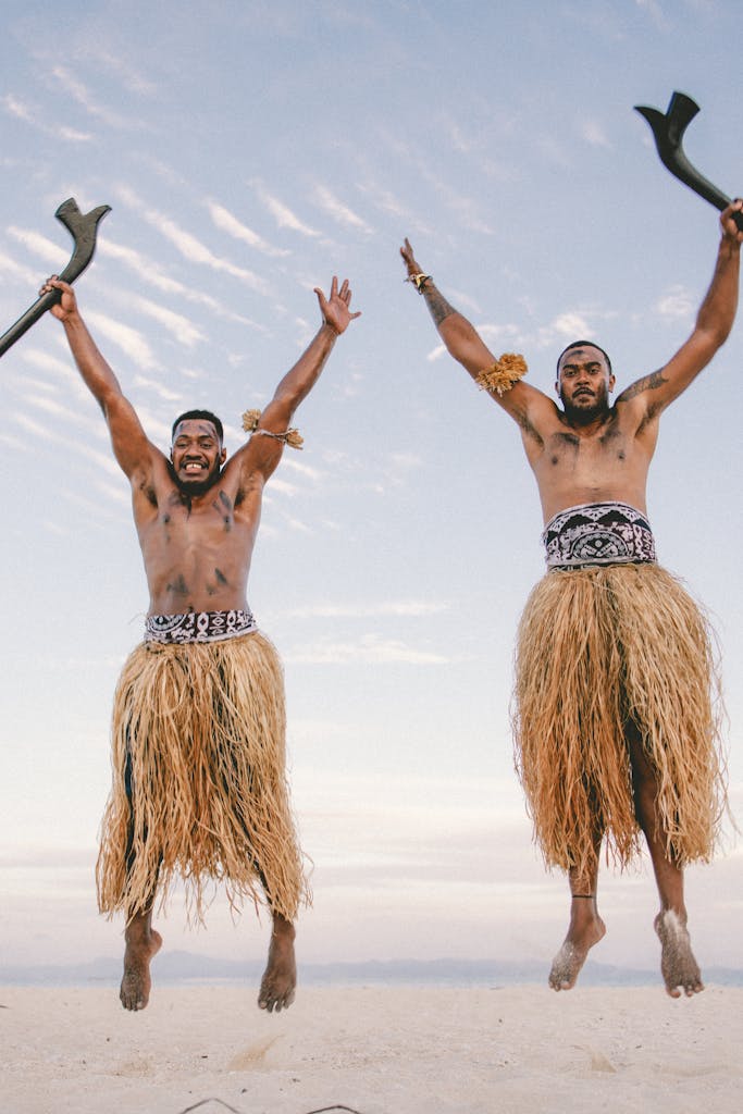 Two Men in Skirts Jumping Against the Sky Background