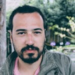 Portrait of a young man with facial hair, outdoors in a natural setting. Serious expression.