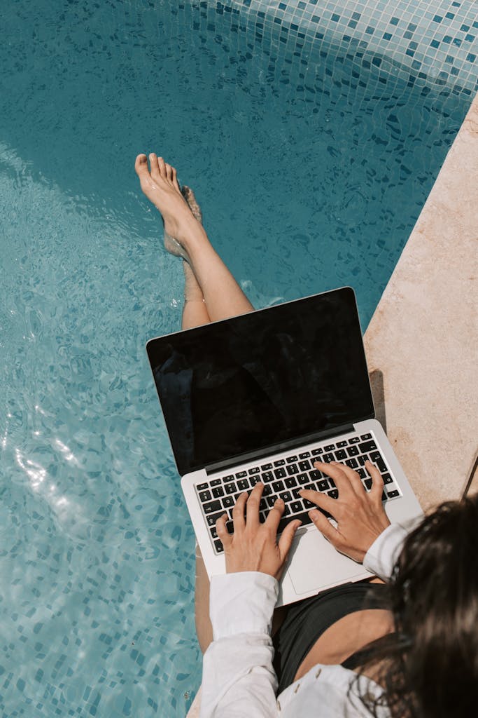 Female travel agent working remotely on a laptop by the poolside, enjoying summer outdoors using travel agent tools.