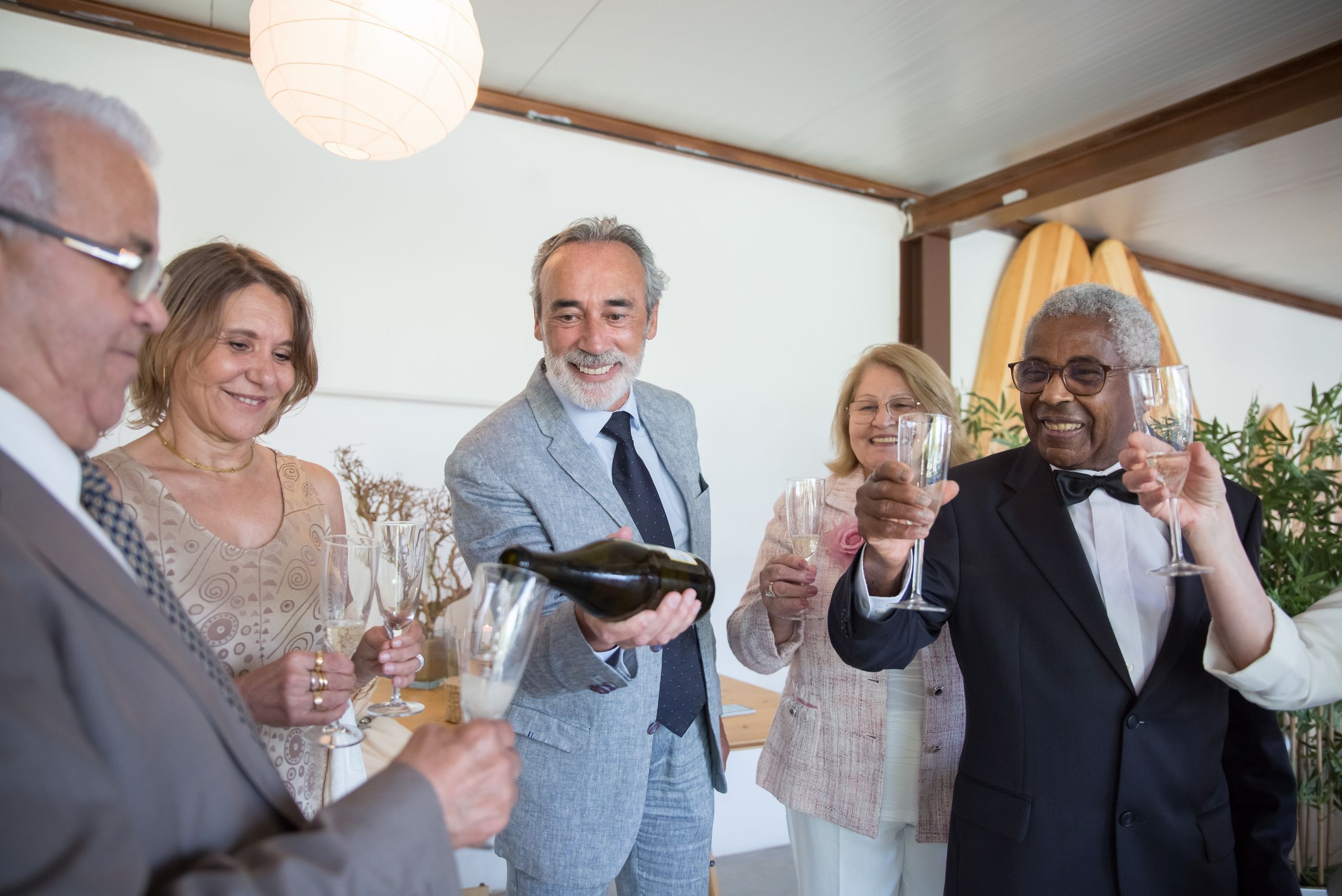 A group of elegantly dressed senior adults celebrating with wine indoors, toasting with smiling faces.