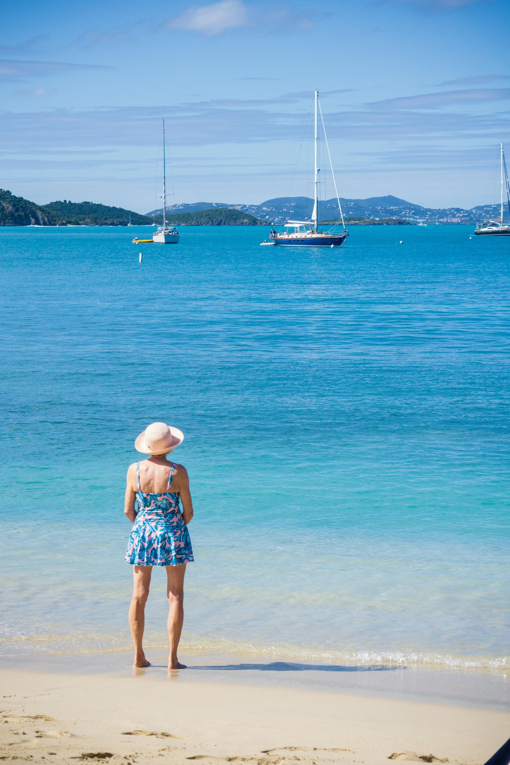 Adult woman in a summer dress gazes at sailboats on a sunny St. John beach.